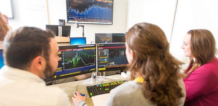 Three students working at a Bloomberg terminal in a classroom